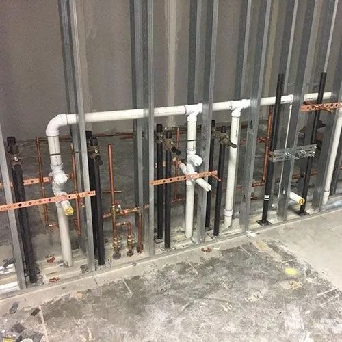Plumbing pipes and copper supply lines installed within metal wall studs at a construction site.