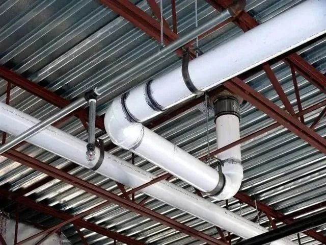 White industrial pipes and black supports suspended from a metal corrugated ceiling and steel joists.