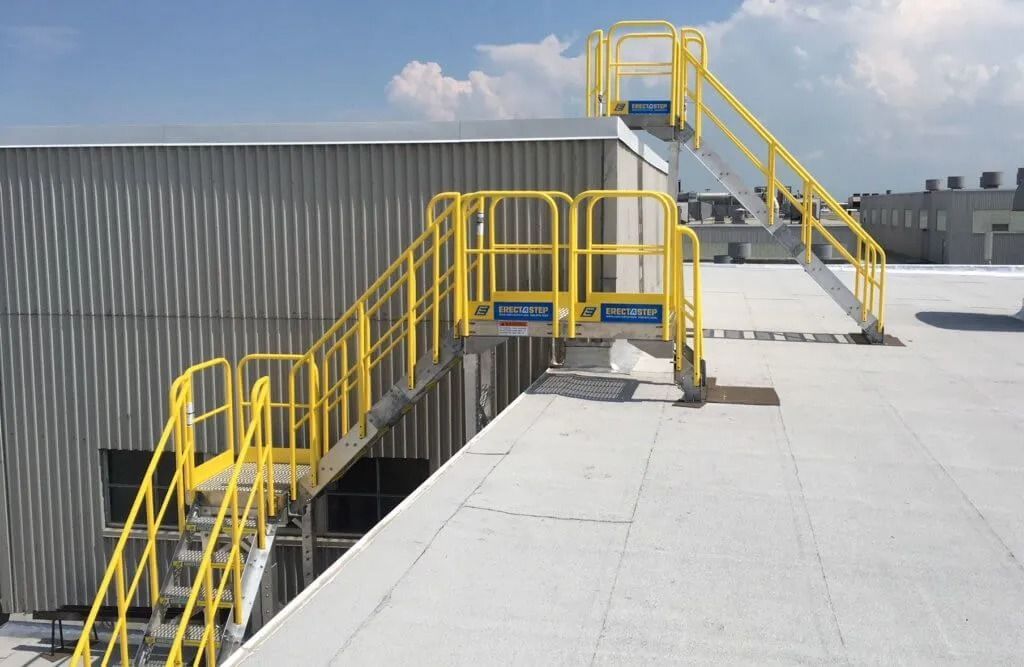 Yellow metal stairs with railings on a white industrial rooftop, providing access to a higher roof level.