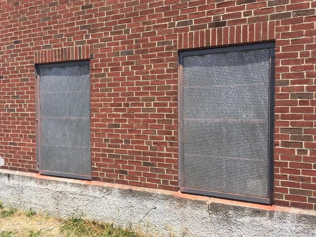 Two rectangular openings in a red brick wall covered with metal security grates above a concrete foundation.
