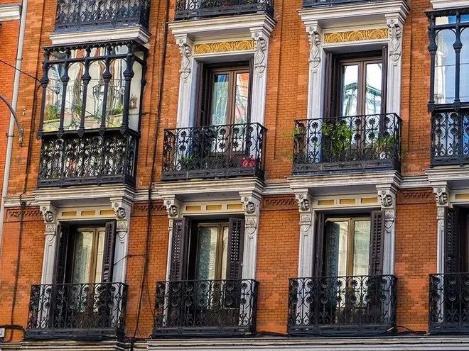 Brick apartment facade with black wrought-iron balconies and tall windows