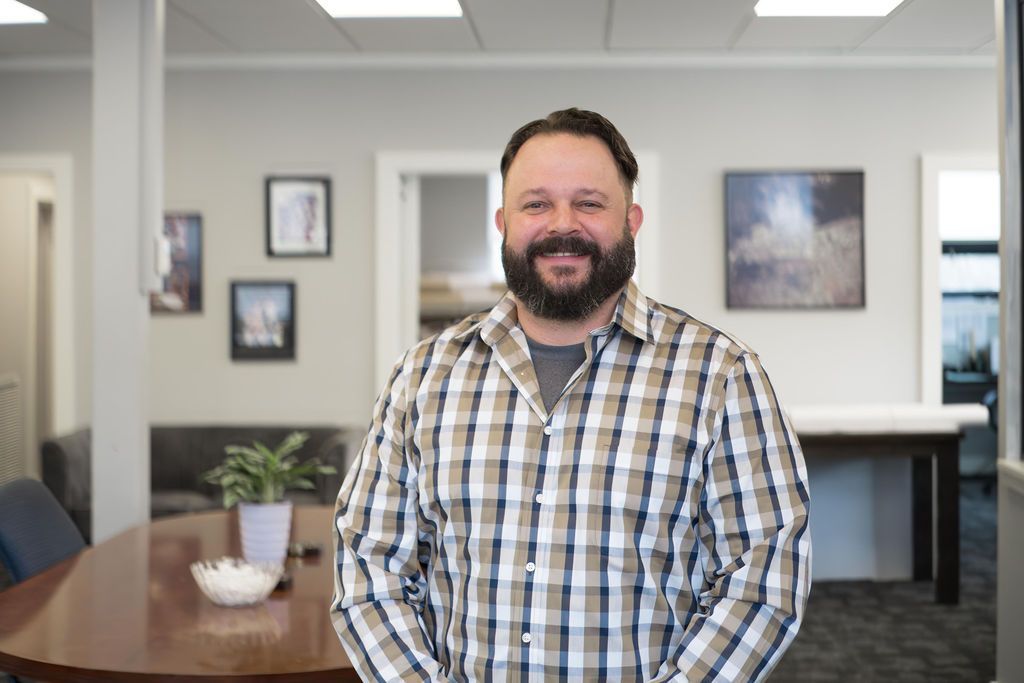 Man smiling in a plaid shirt standing in an office conference room