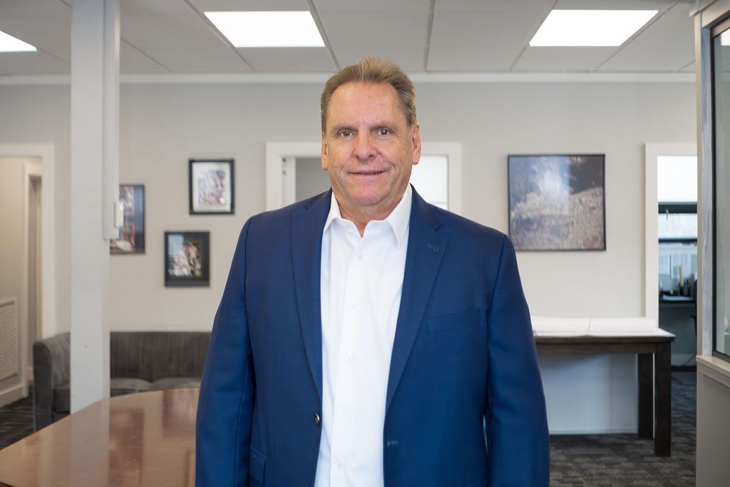 Man in blue blazer standing in an office hallway with framed art and a reception desk behind him