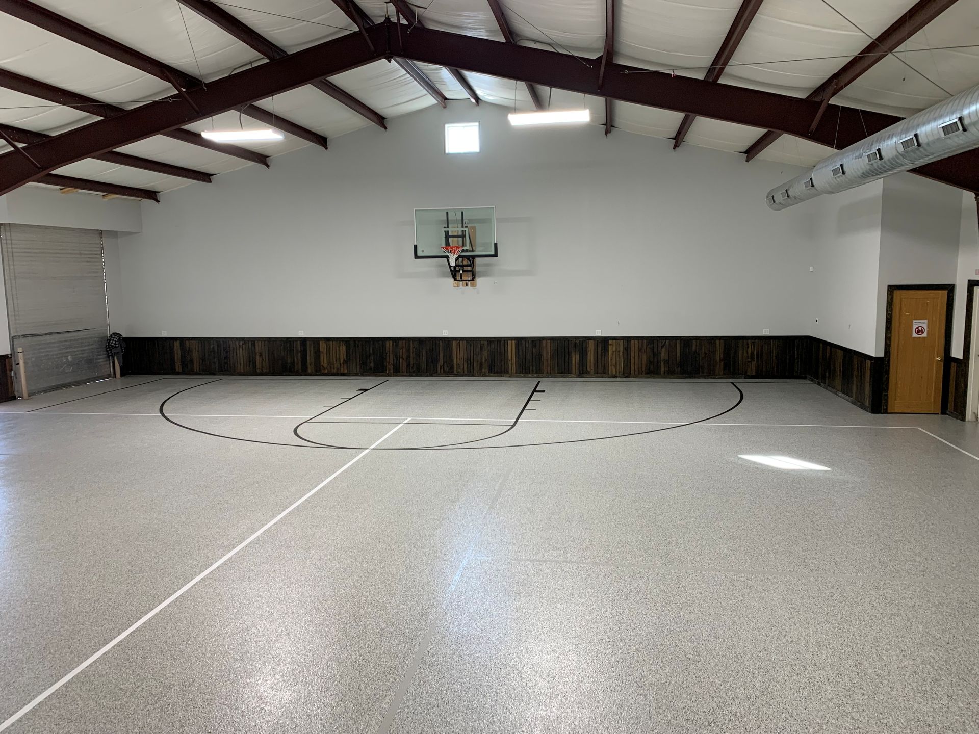 Empty indoor gymnasium with a basketball hoop and speckled floor, viewed from midcourt.