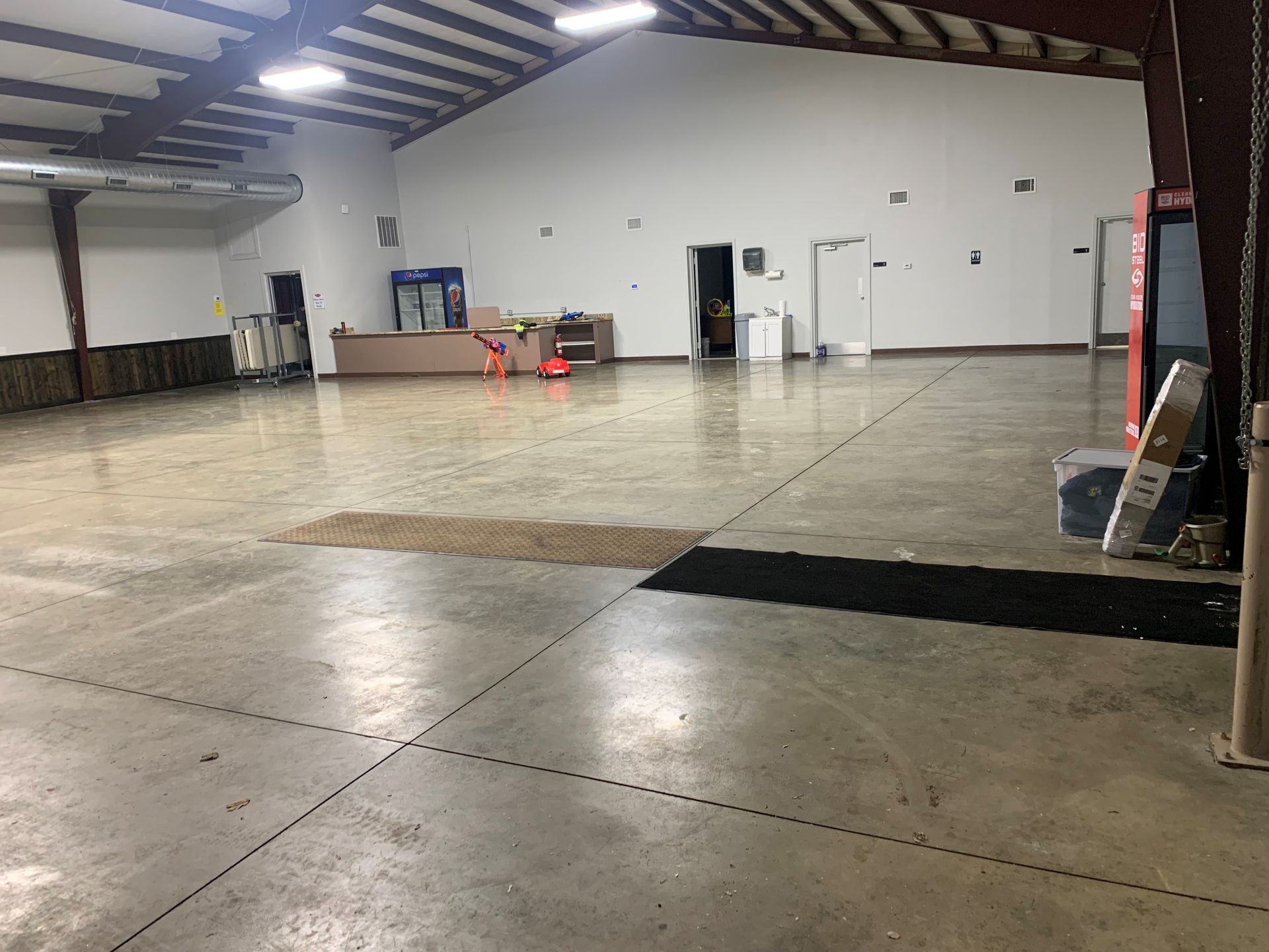 Empty warehouse interior with concrete floor, exposed beams, and a few orange cones near the back wall