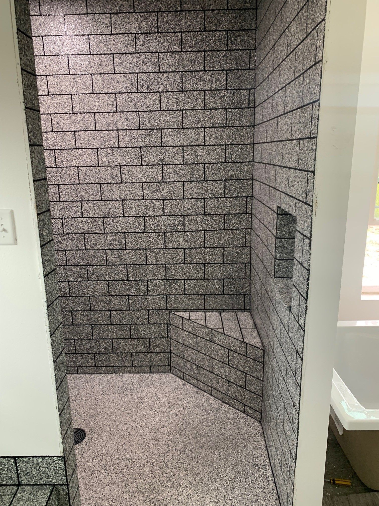 Small tiled shower with gray brick-pattern walls and a built-in bench niche, viewed from the doorway