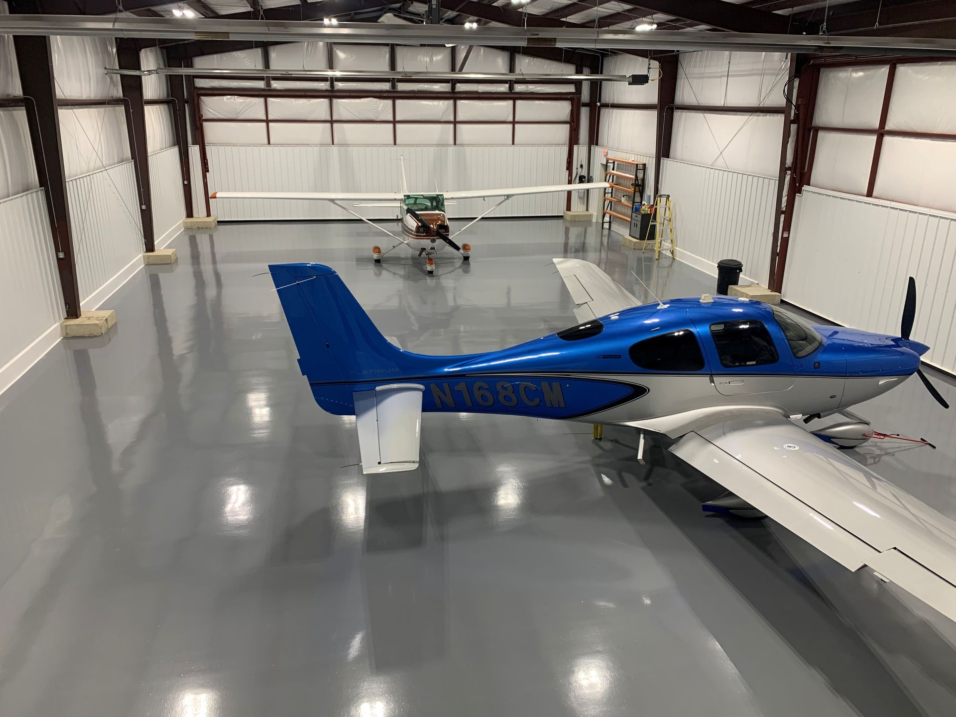 Blue-and-white single-engine airplane parked inside a spacious hangar on a polished gray floor
