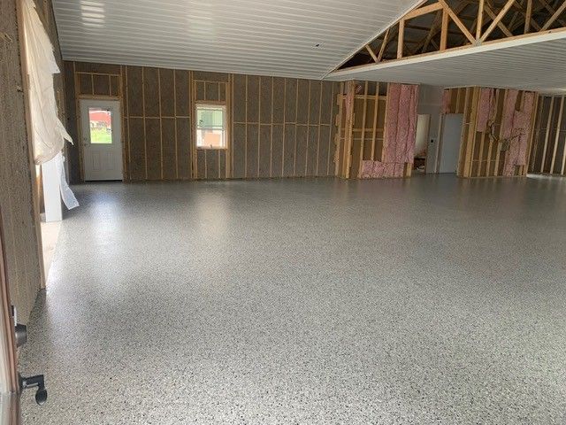 Empty unfinished room with gray speckled floor, exposed wall framing, and small windows.