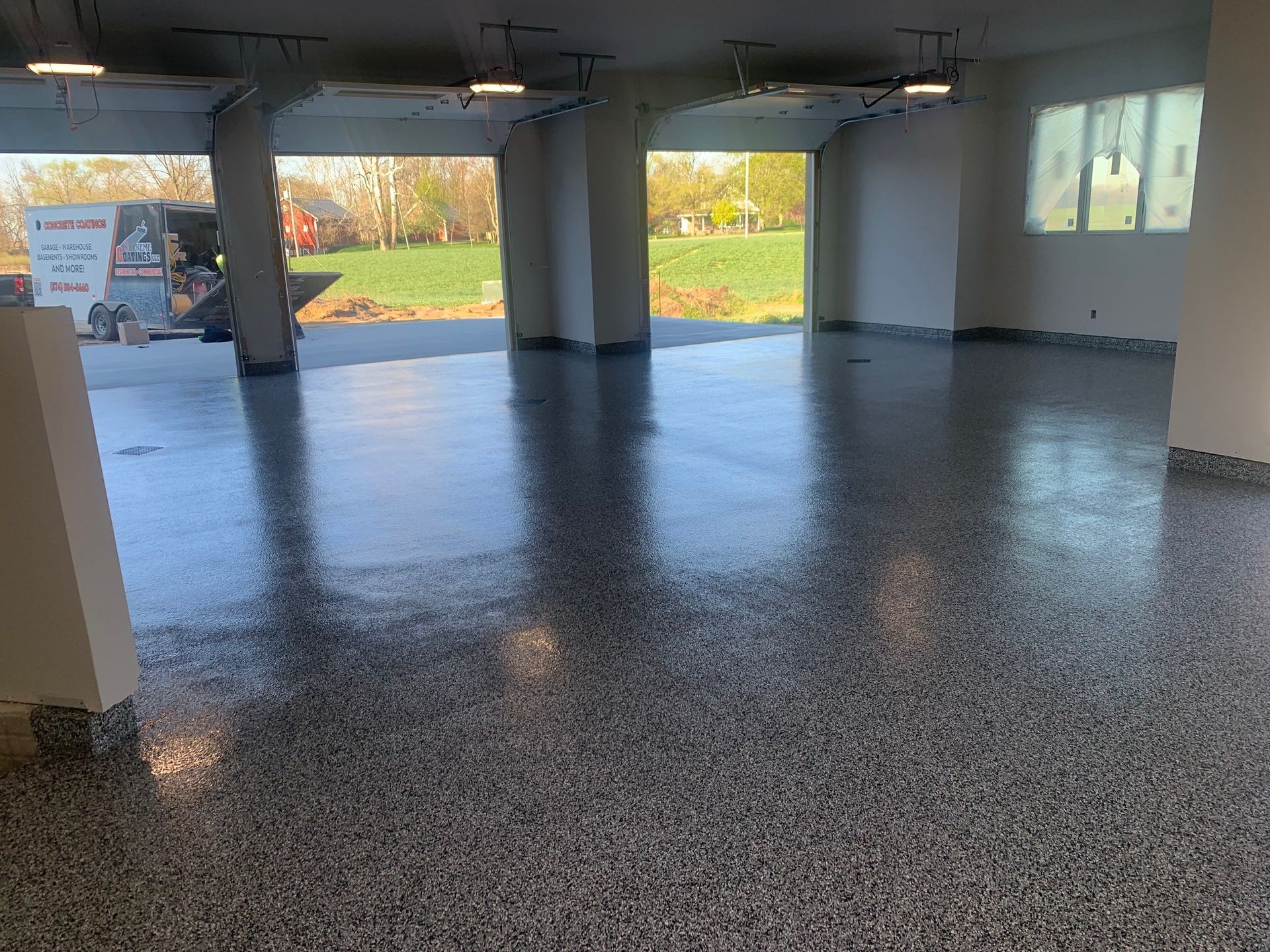 Empty garage with a glossy gray floor, open bays, and a view of greenery outside.