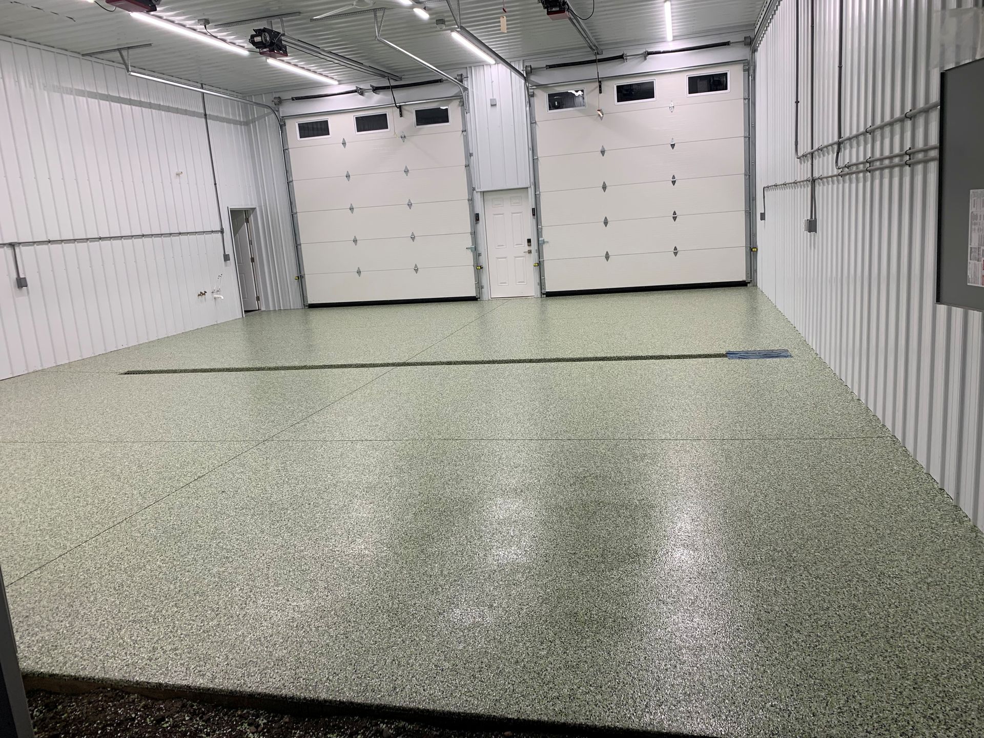 Empty garage with speckled epoxy floor and closed white doors.