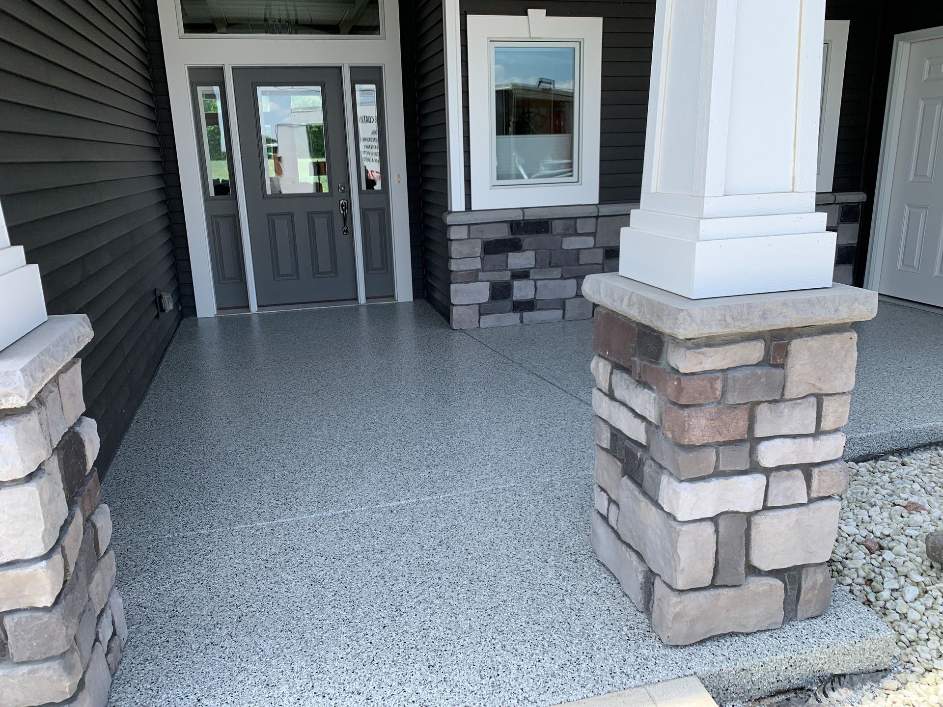 Front porch with gray double doors, white columns, and stone-accented pillars on a house exterior