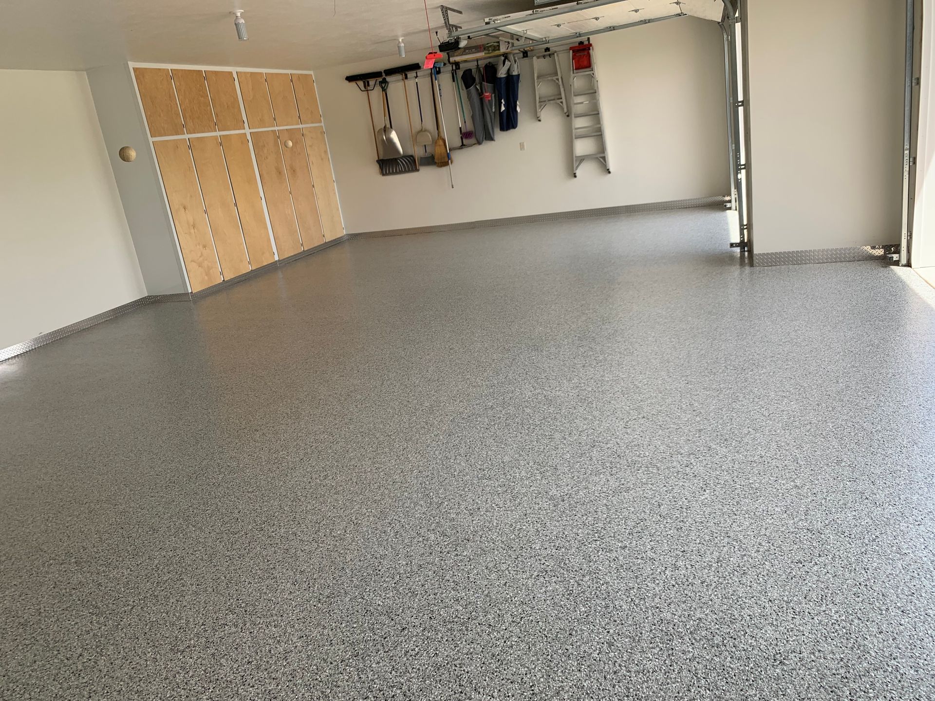 Empty garage with speckled epoxy floor, beige cabinets, and storage racks on the wall.
