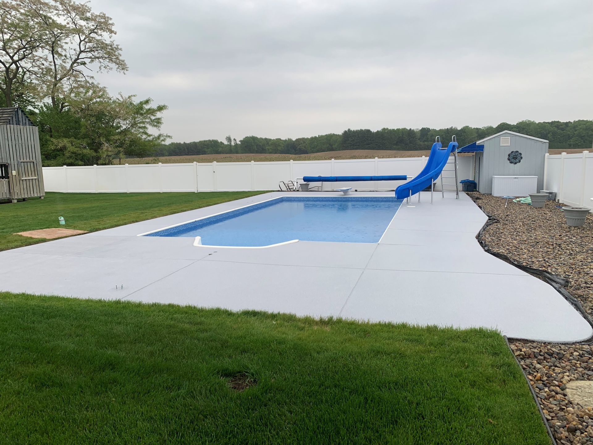 Backyard swimming pool with blue slide and white concrete deck beside a lake