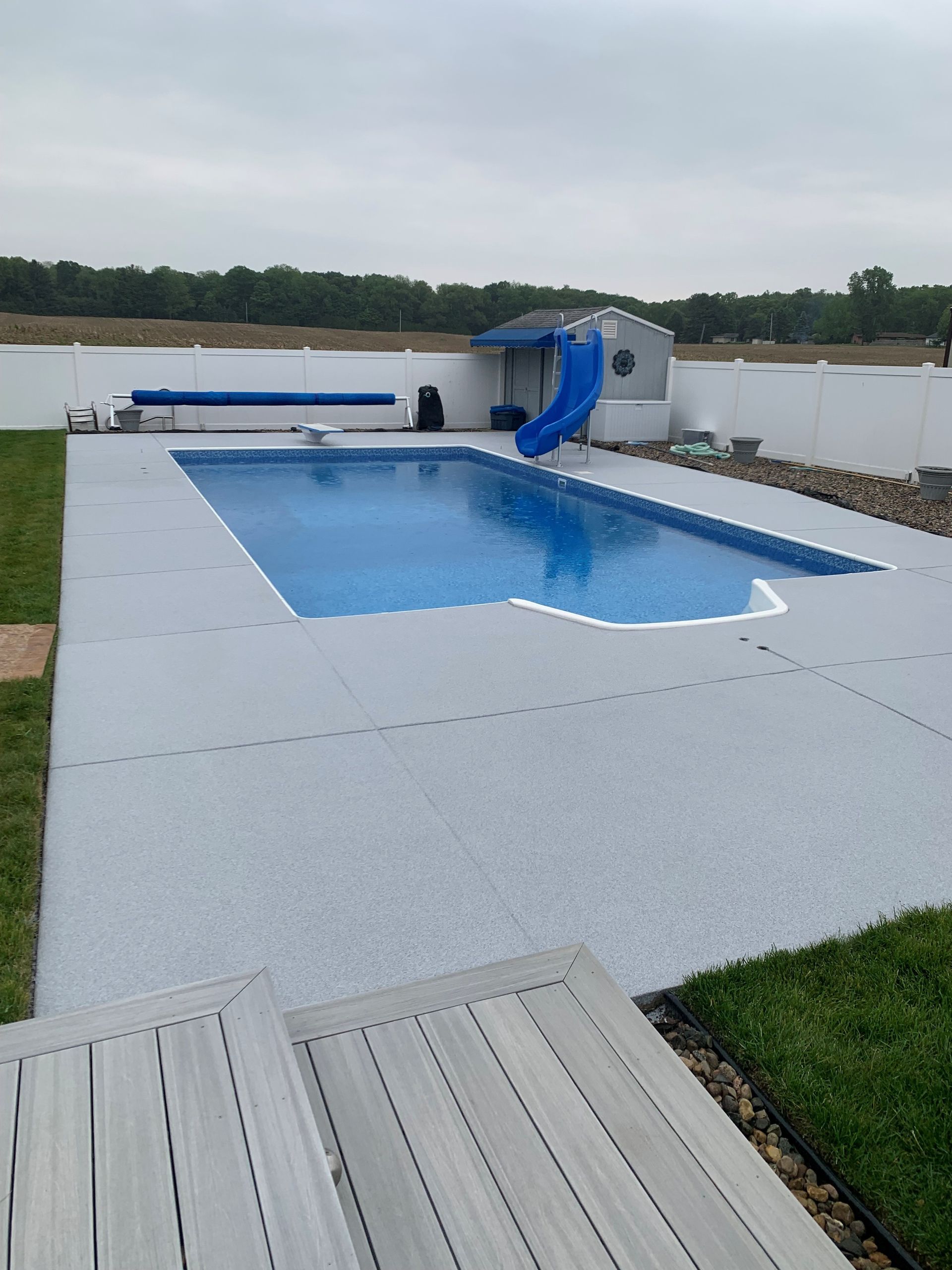 Backyard swimming pool with a blue slide beside a lake under an overcast sky