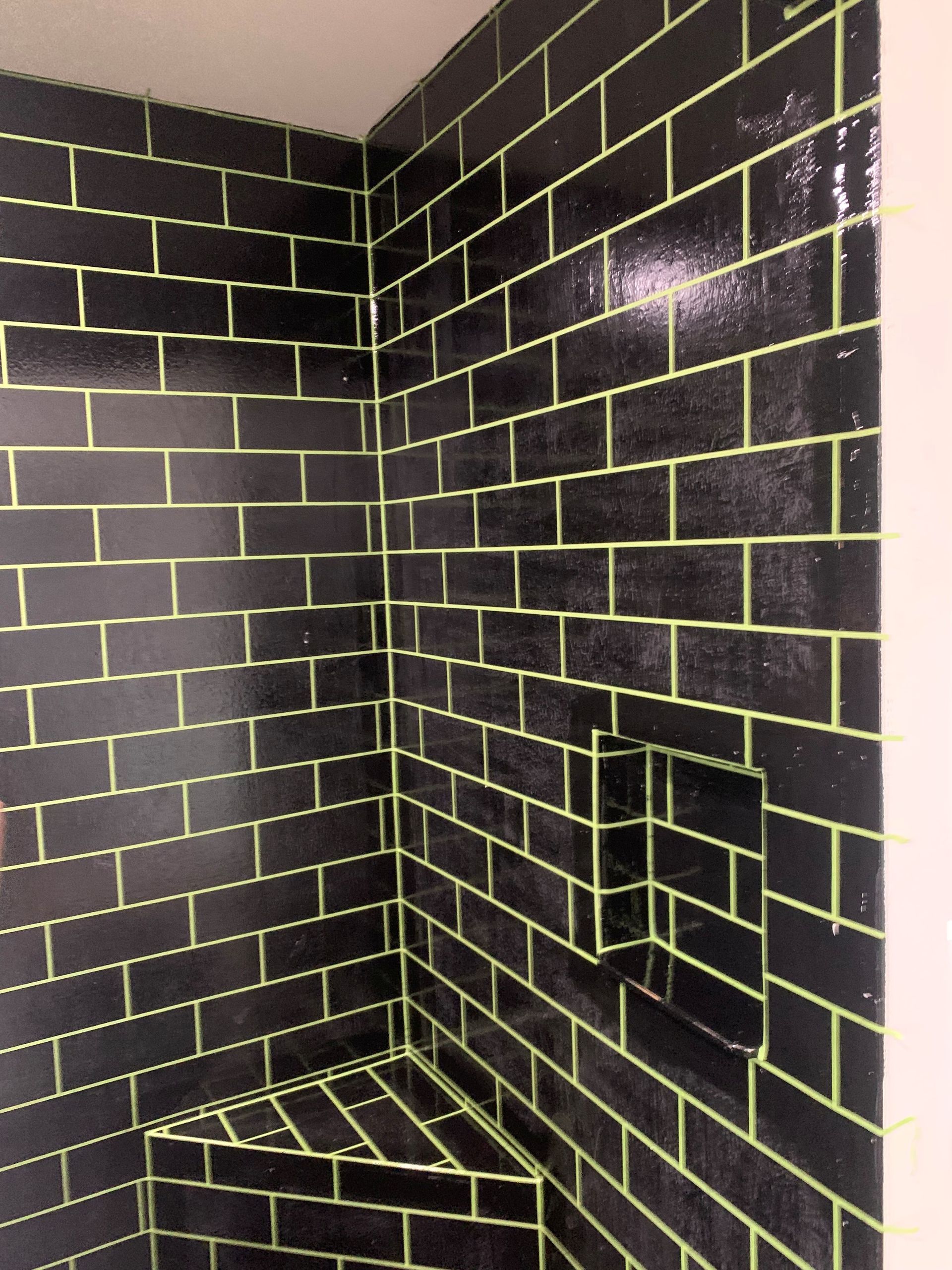 Black-tiled shower corner with yellow grout and built-in soap shelf