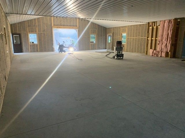 Empty unfinished interior with exposed framing, concrete floor, and bright doorway at the far end