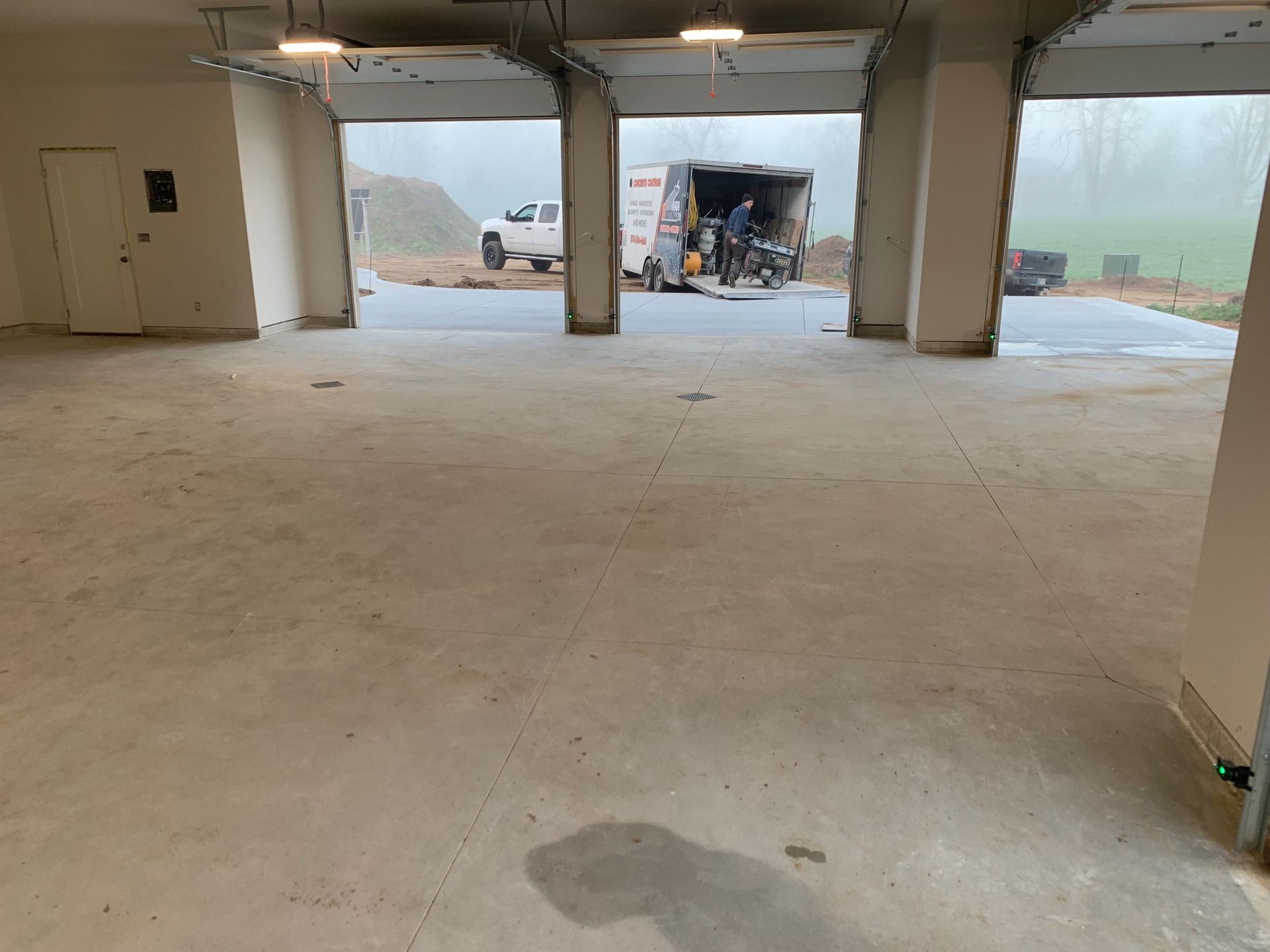 Empty concrete garage with open bays, a white van outside, and construction materials in the distance.