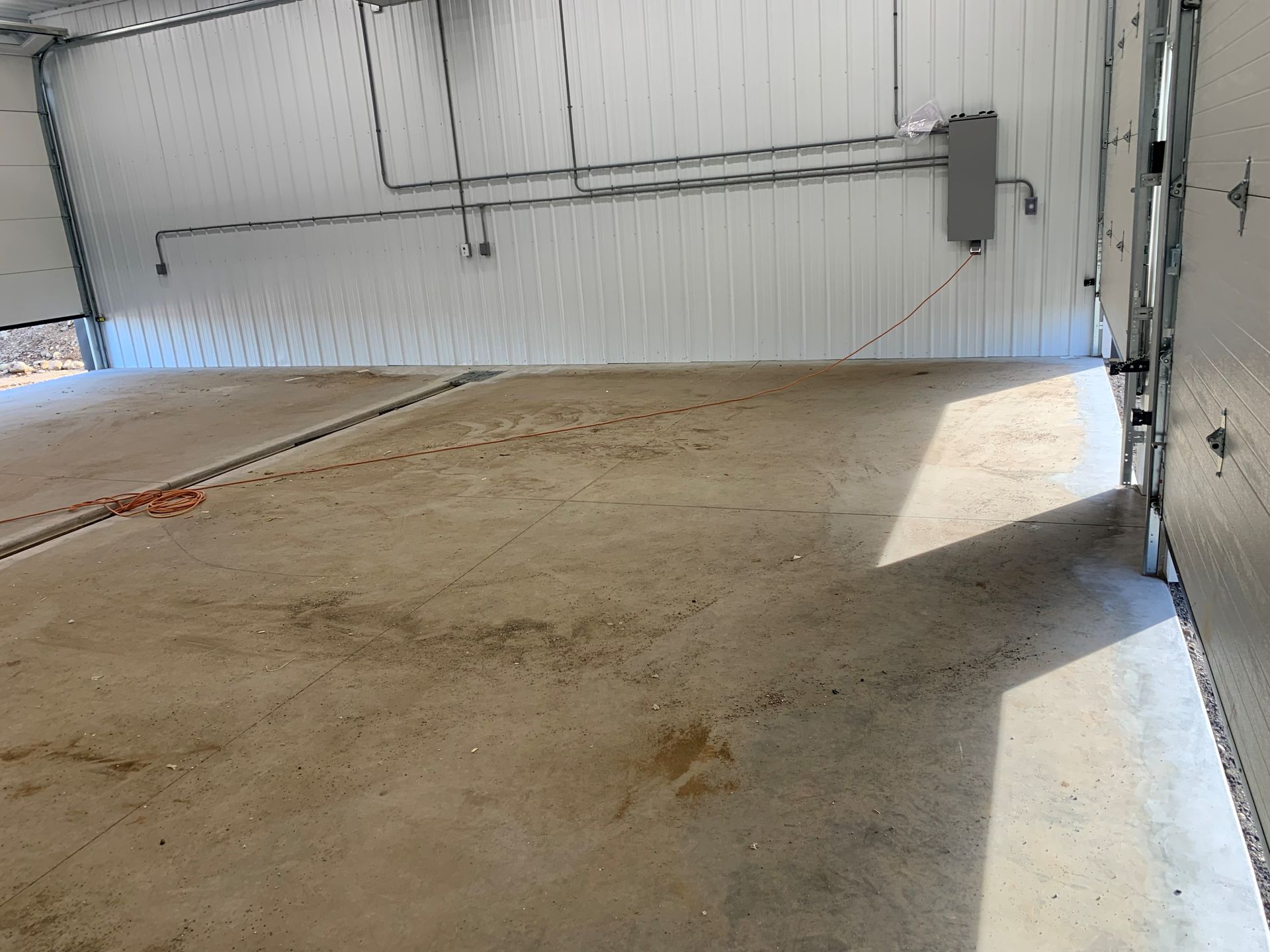 Empty warehouse interior with concrete floor and open garage door casting bright sunlight inside