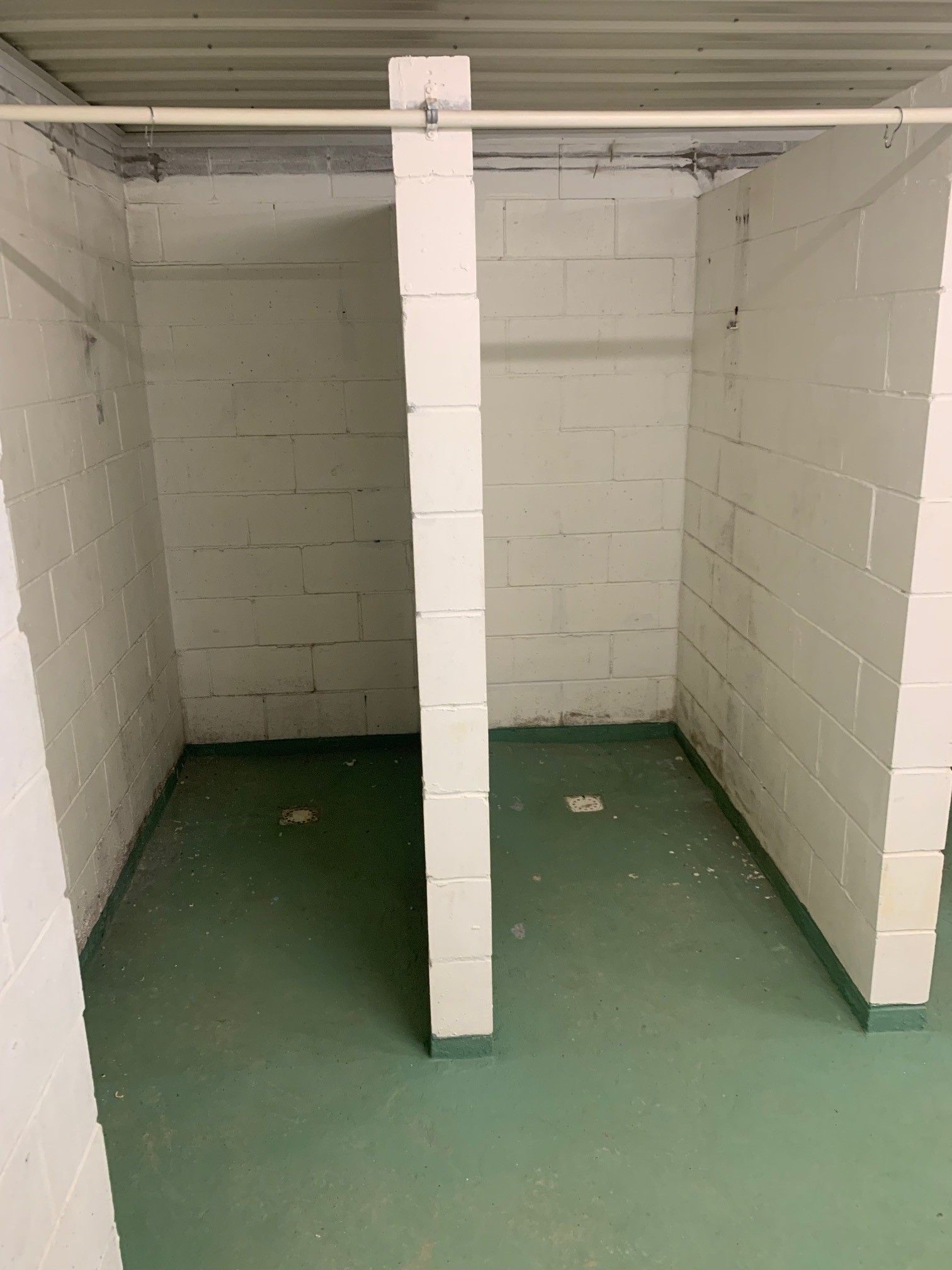 Empty white-walled room with green floor and a white support pillar in the center