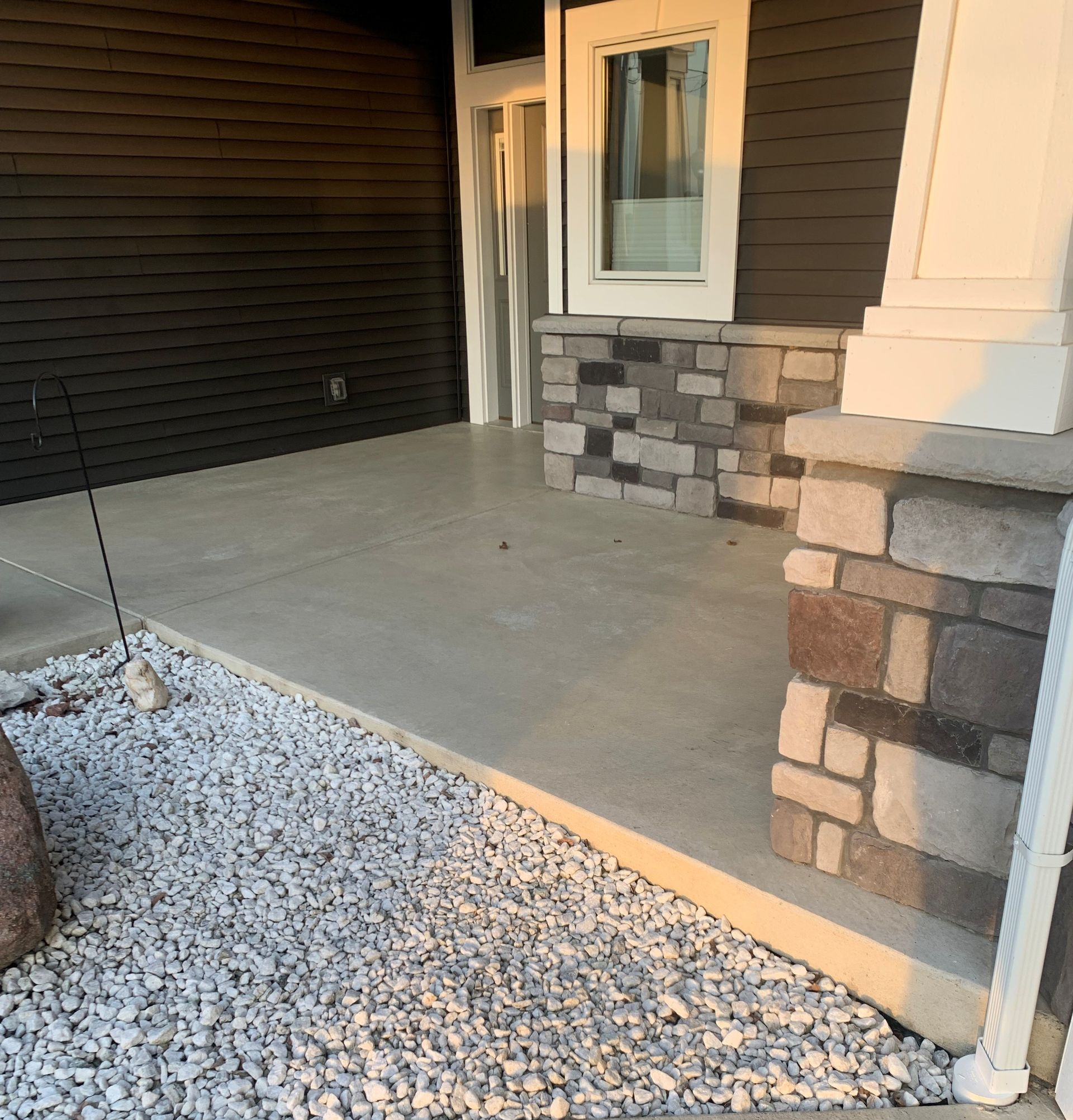 Front porch with concrete ramp, white gravel bed, and stone-clad columns beside the entryway