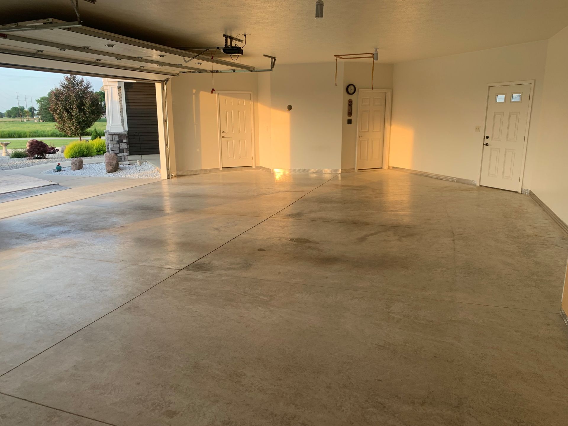 Empty garage with concrete floor, open door to driveway, and closed white interior doors in warm sunlight