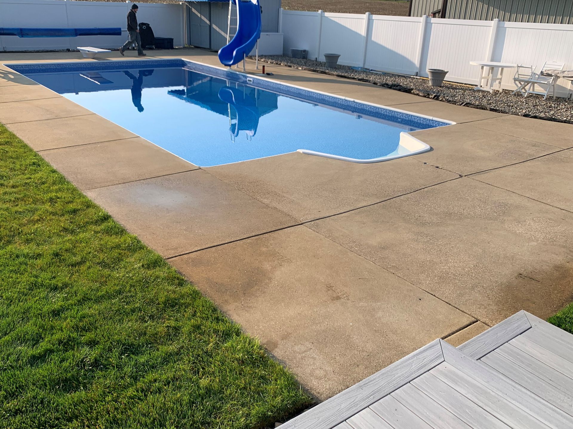 Backyard swimming pool with a blue slide, surrounded by concrete patio and green lawn.