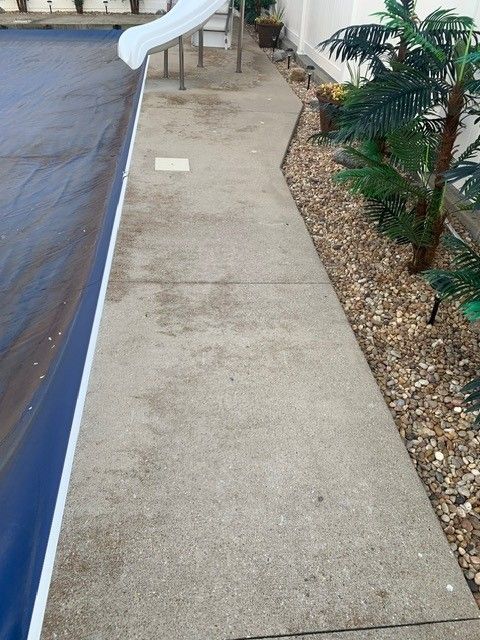 Narrow concrete walkway beside a covered pool, with a white slide and landscaped rocks along the edge.