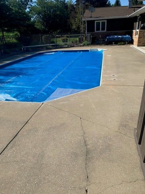 Backyard swimming pool covered with a bright blue tarp beside a concrete patio