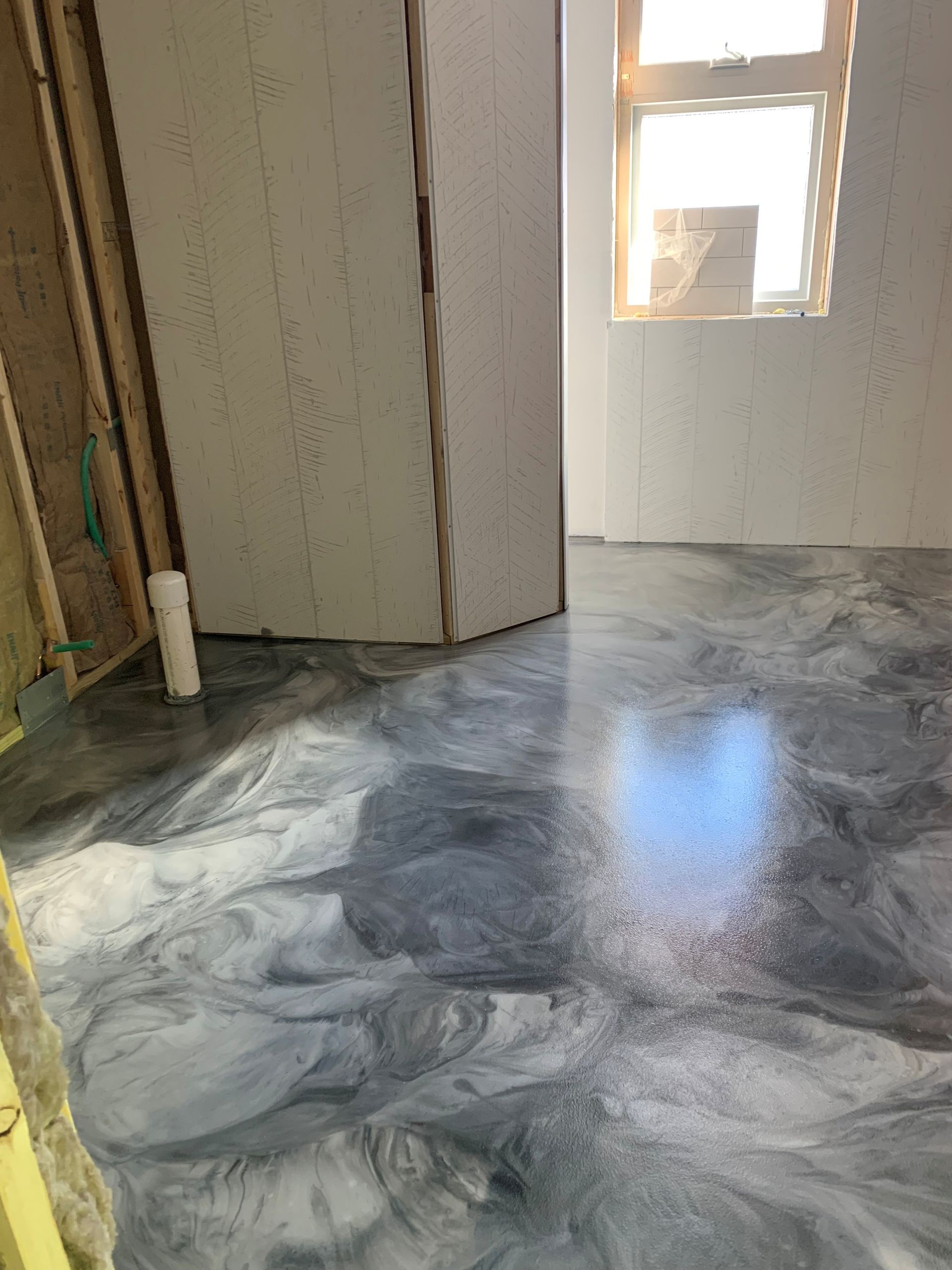 Empty room under renovation with wet gray concrete floor and unfinished walls, sunlight from a small window.