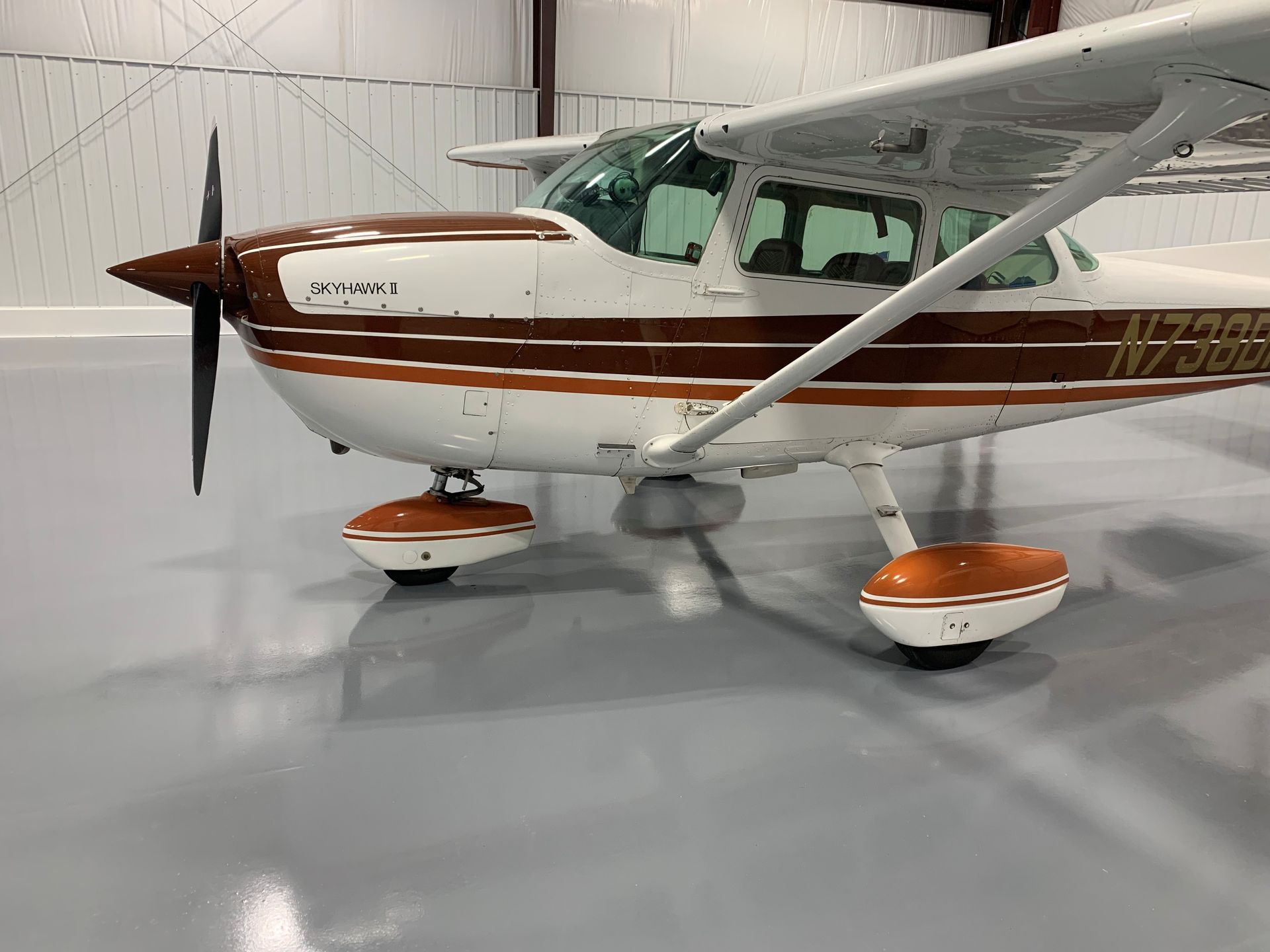 Small white and brown propeller airplane parked indoors on a polished hangar floor.