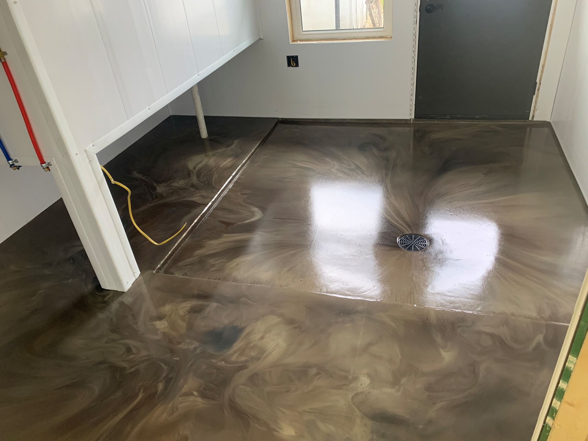 Empty room with glossy brown floor coating, white walls, window, and staircase landing.