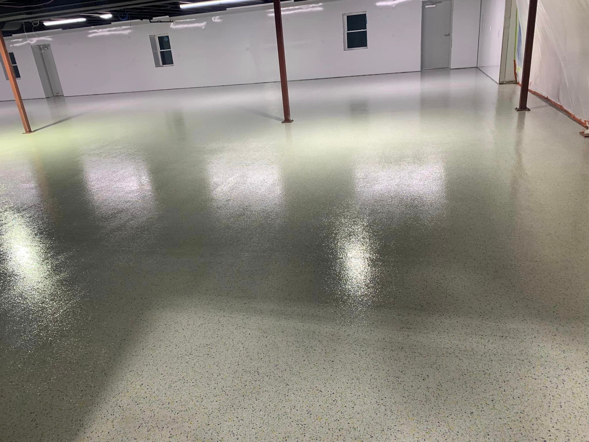 Empty polished concrete floor in a bright industrial room with white walls and red support posts