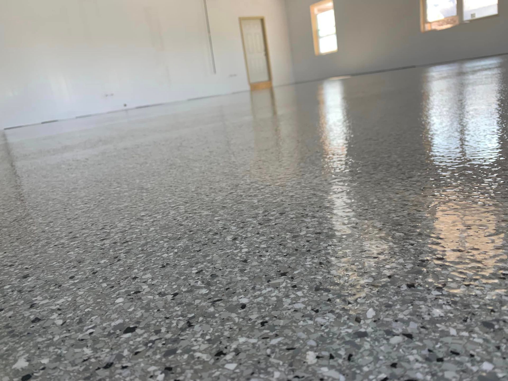 Empty polished room with speckled gray floor and windows reflecting light.