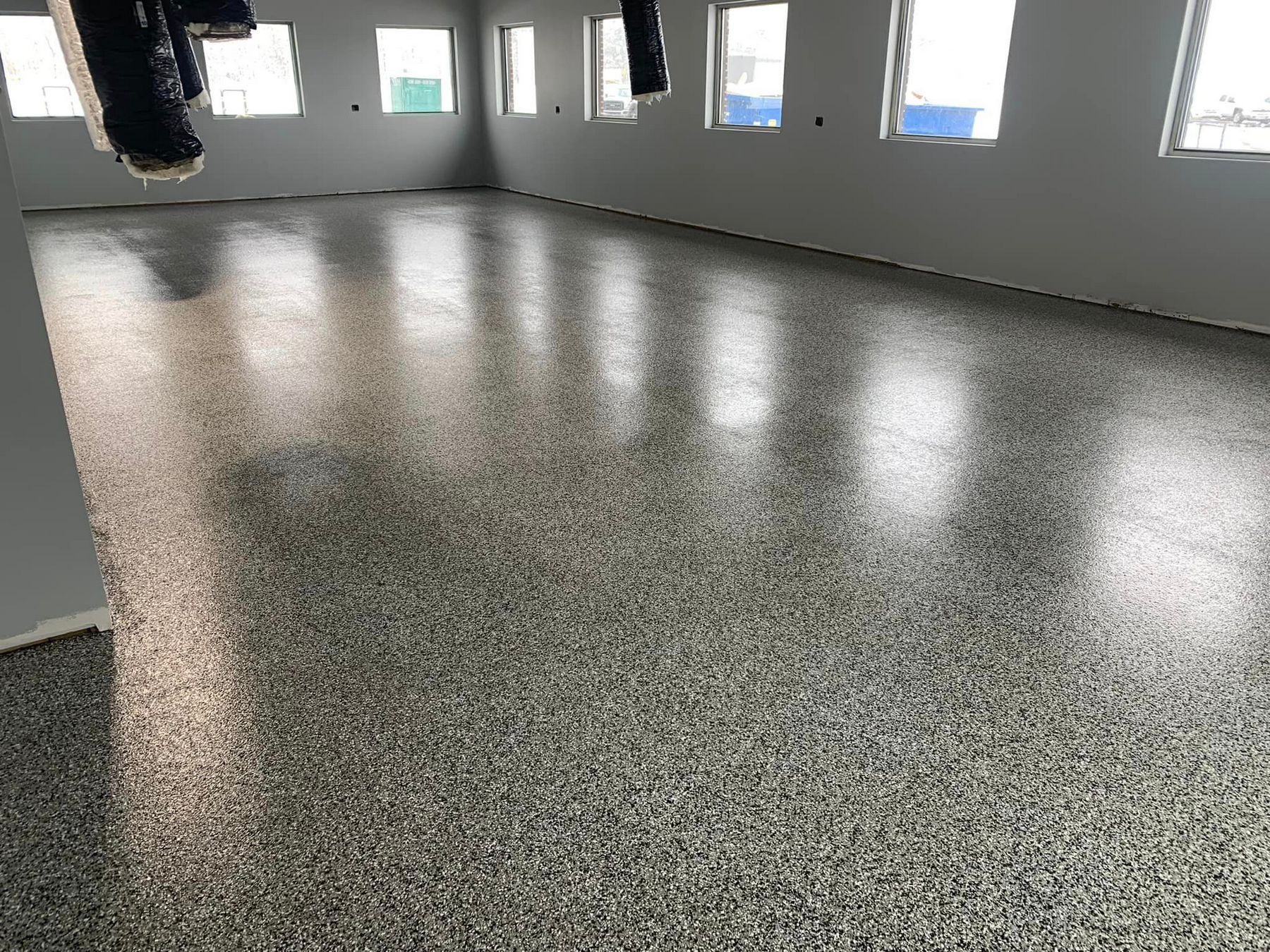 Empty room with glossy speckled floor and windows along the wall reflecting light