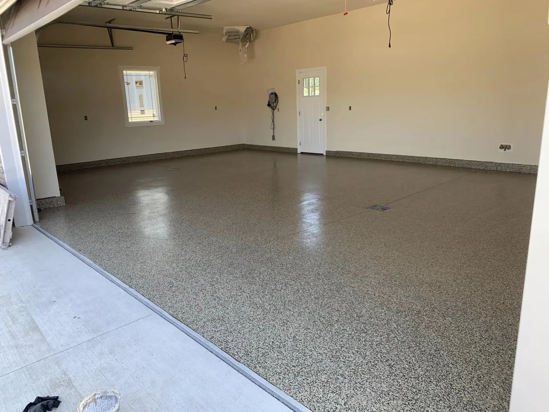 Empty garage with speckled epoxy floor, beige walls, and a side door and window.