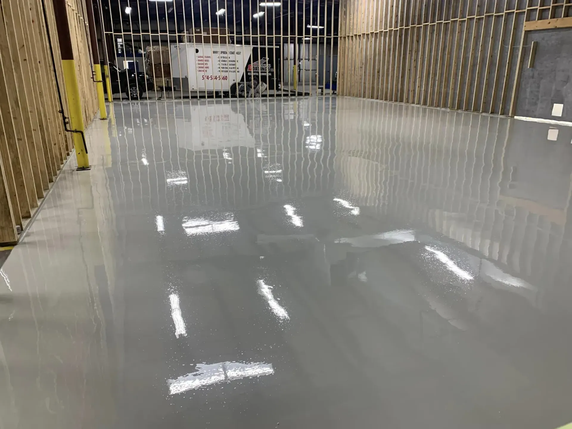 Empty glossy warehouse floor with overhead lights reflecting, metal racks lining the sides
