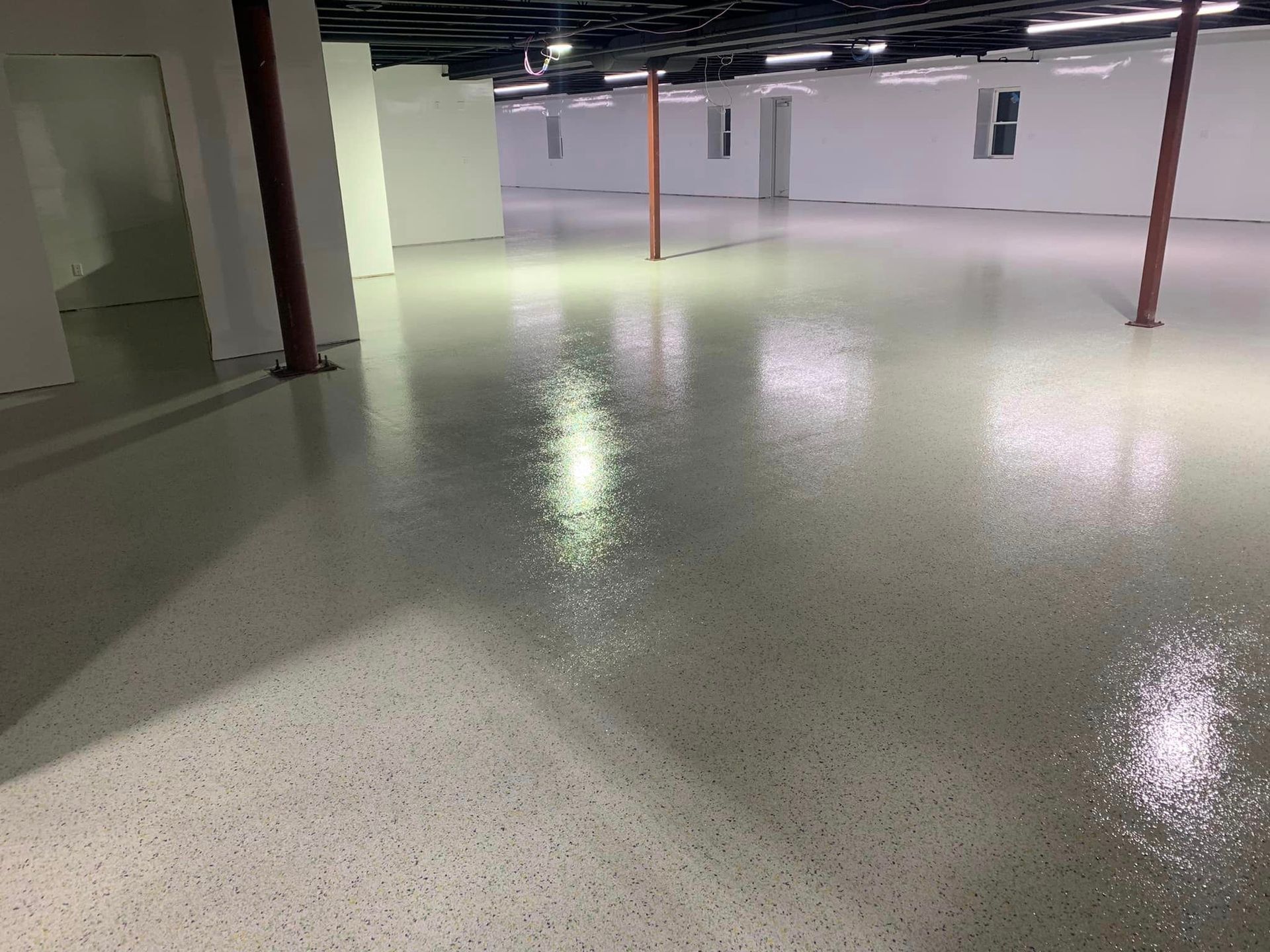 Empty indoor basement with glossy speckled floor and support columns under fluorescent lights