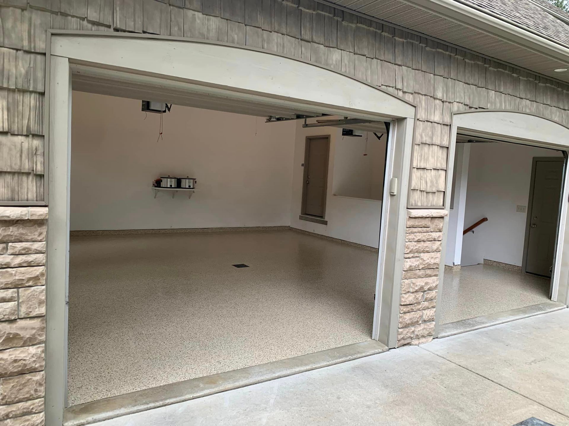 Two open garage bays in a beige stucco building, showing empty carpeted interiors and a concrete driveway.