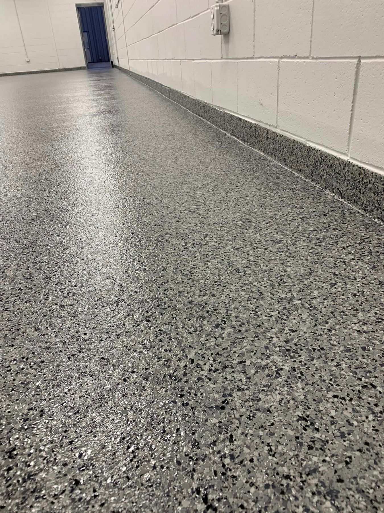 Long speckled hallway with white cinderblock walls and a blue door at the end