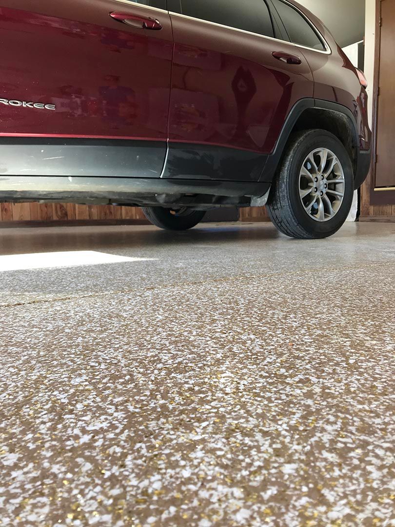 Maroon SUV parked in a garage, seen low from the side with a speckled floor.