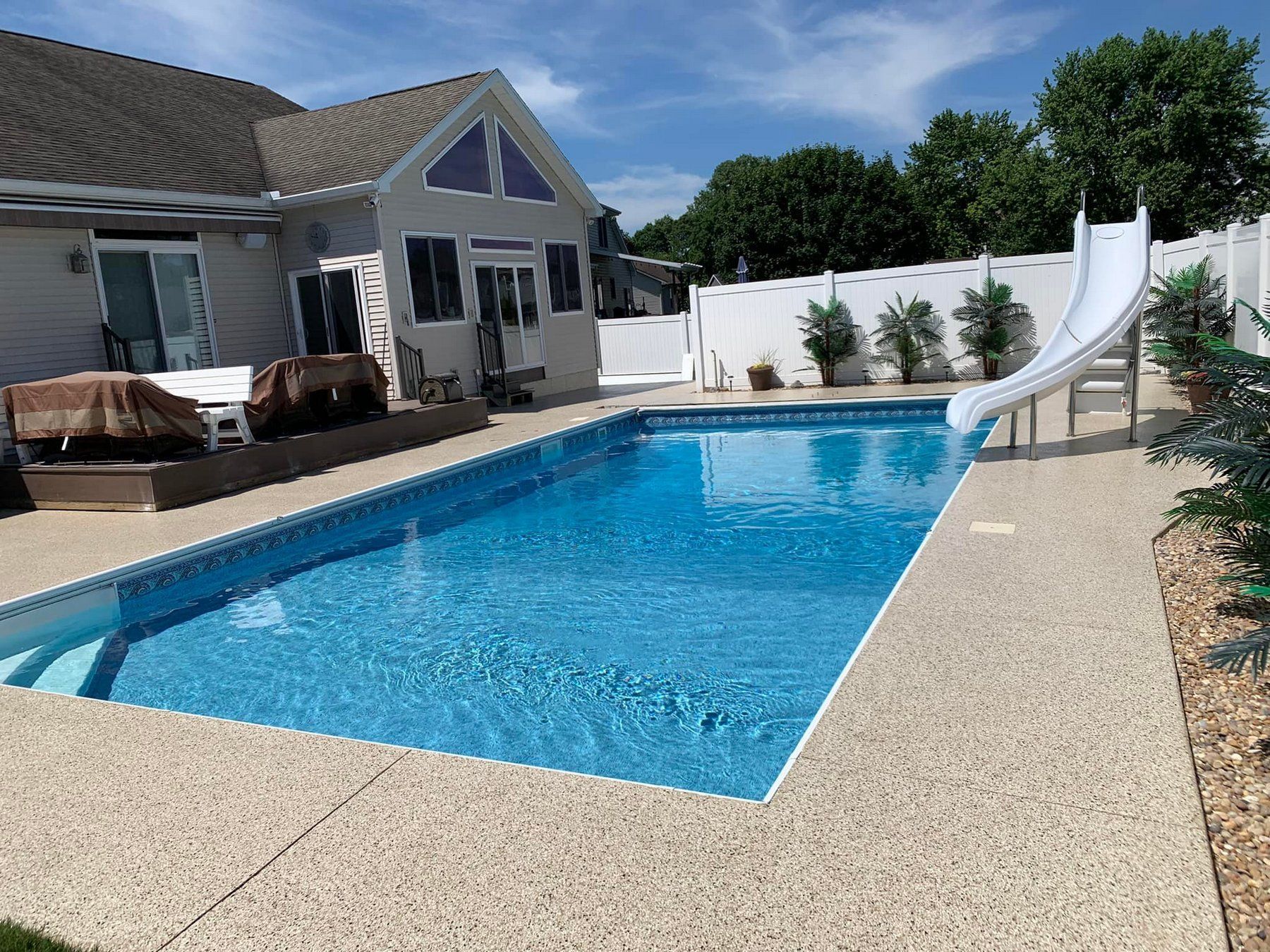 Backyard swimming pool with blue water, white slide, and house patio beside it