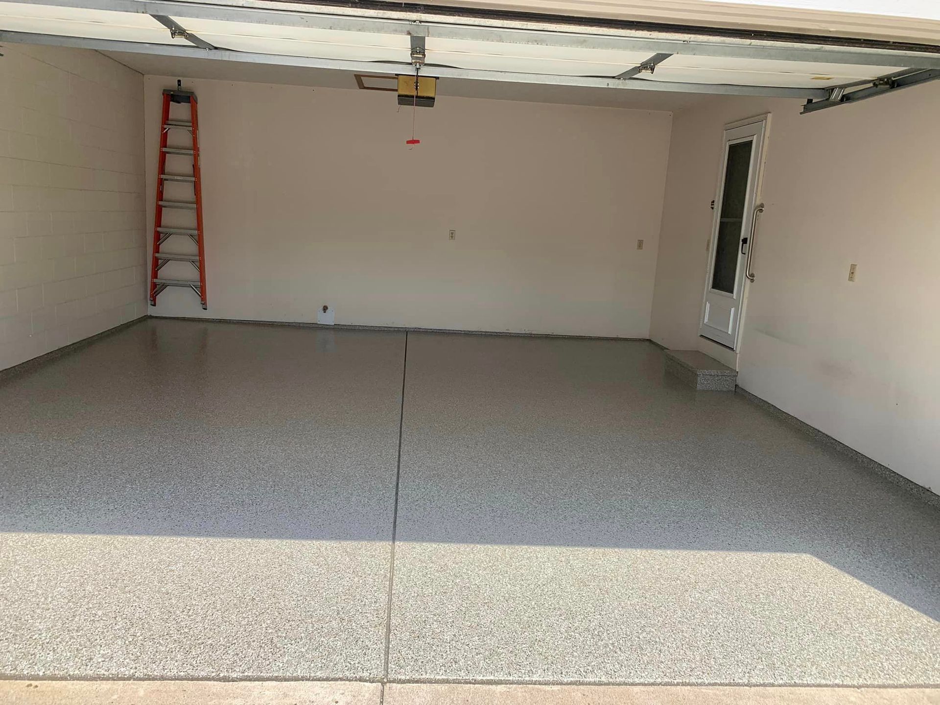 Empty garage with white walls, gray floor, and a red ladder near the back left corner.