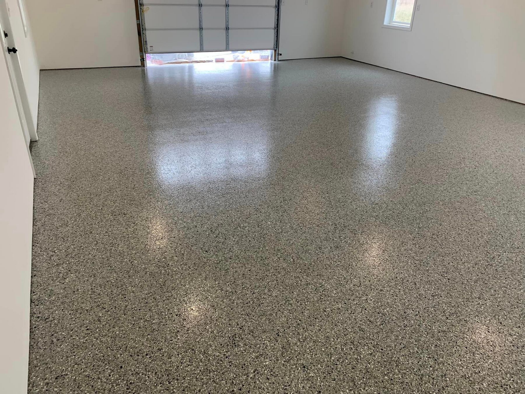 Empty garage with speckled epoxy floor and closed overhead door.