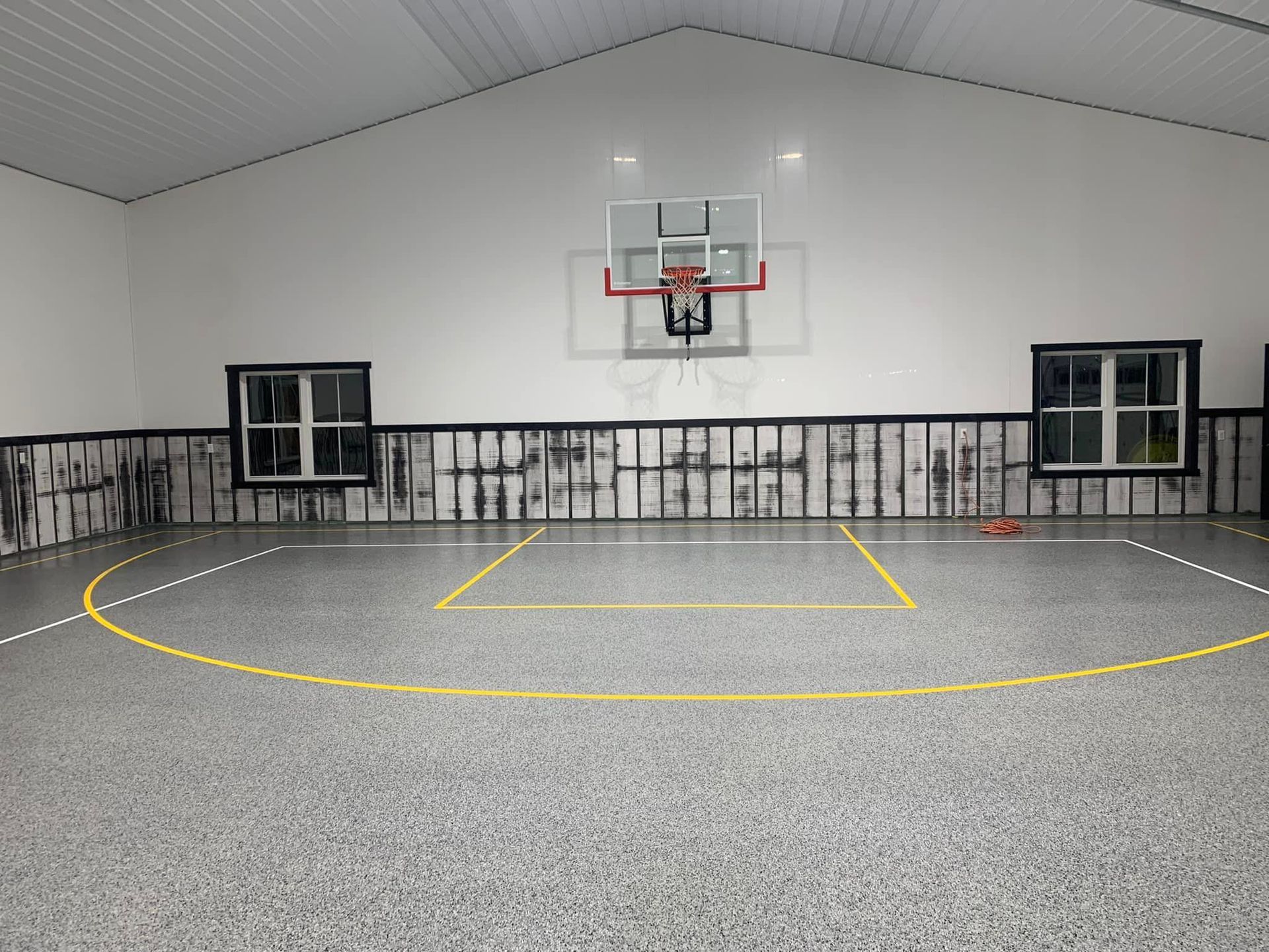 Indoor basketball court with yellow court lines, hoop, and gray walls