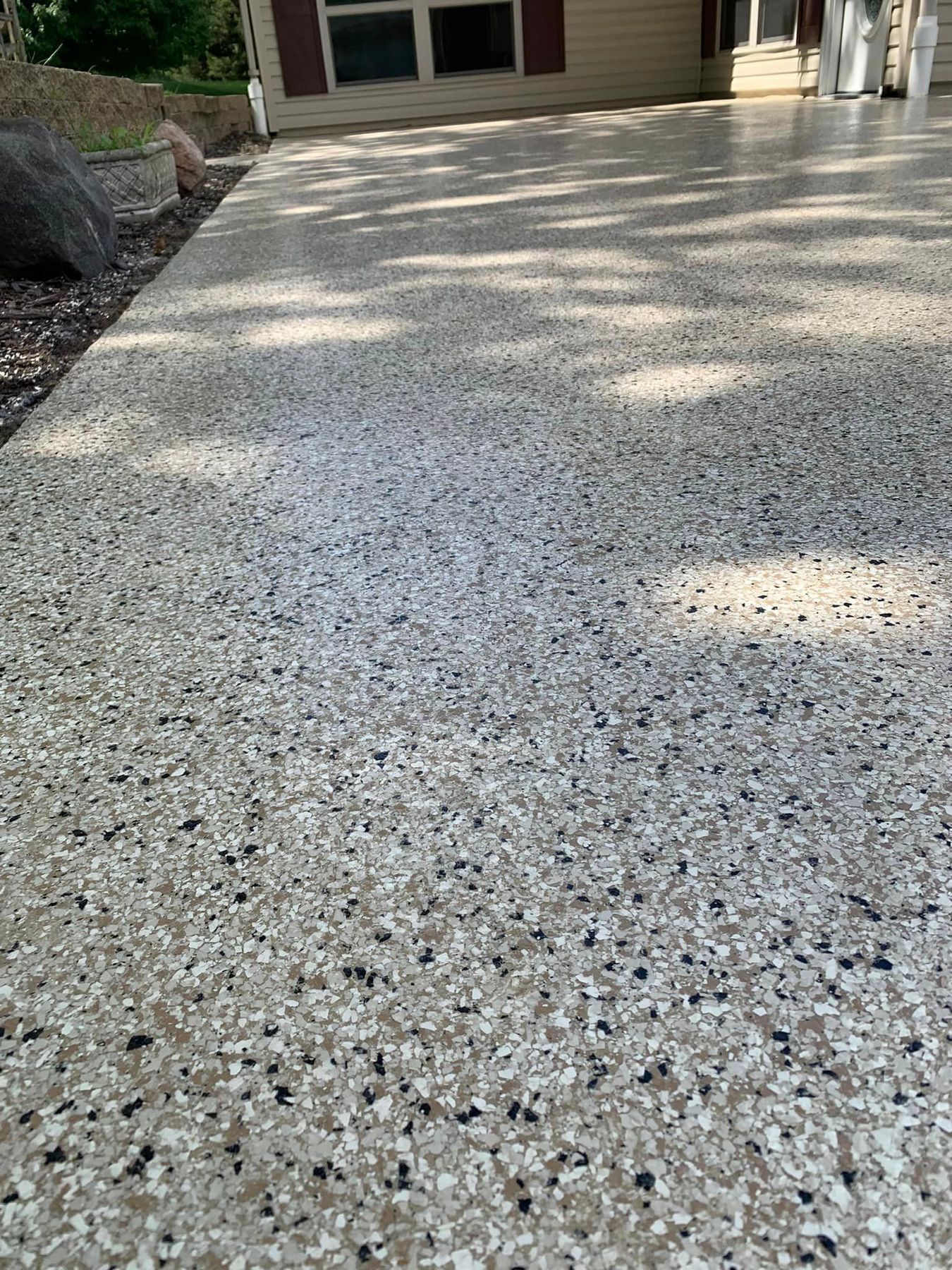 Speckled concrete driveway leading to a house entrance, with sunlight and tree shadows.