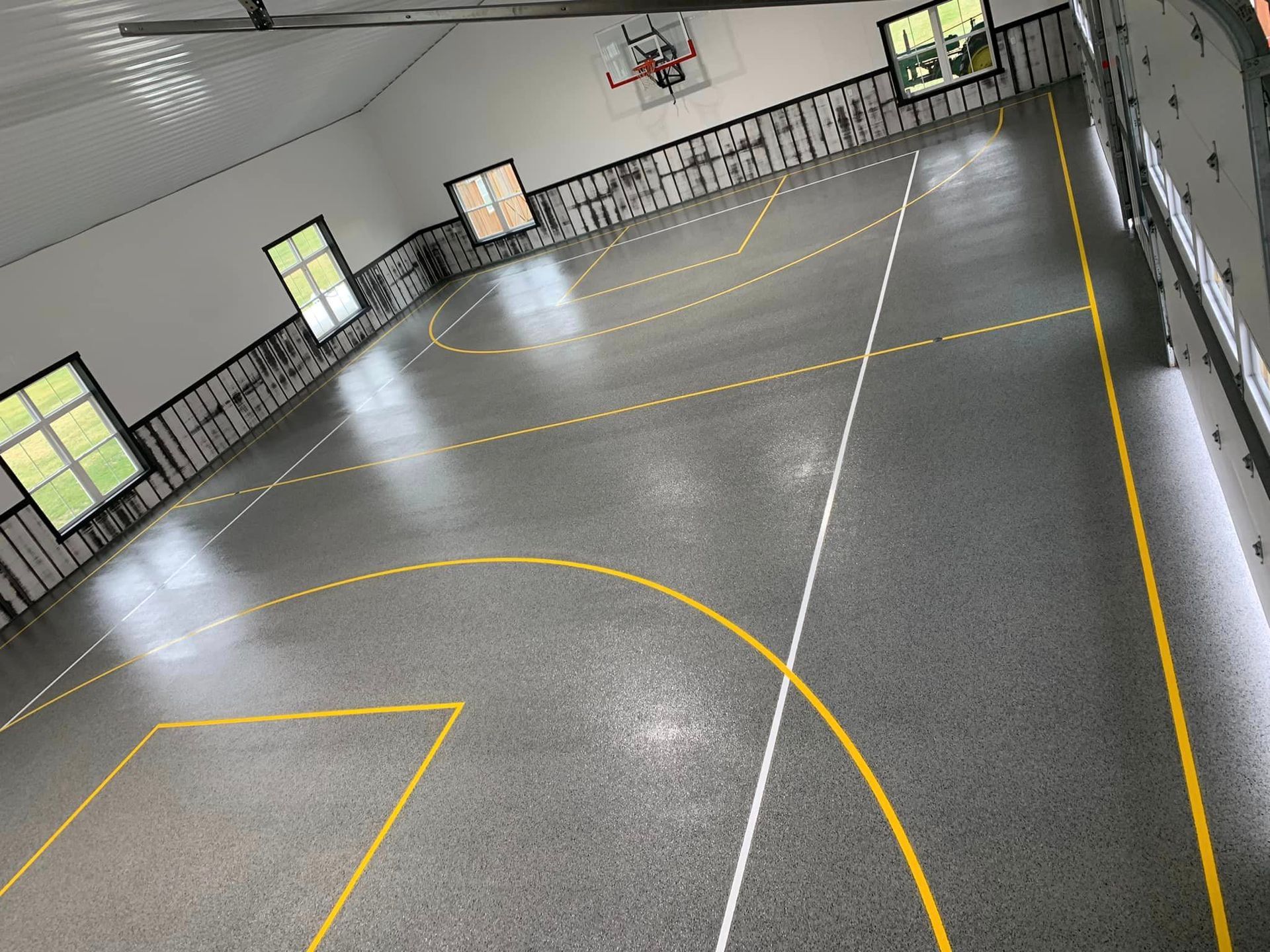 Indoor sports court with glossy gray floor, yellow lines, and black railings along the walls.