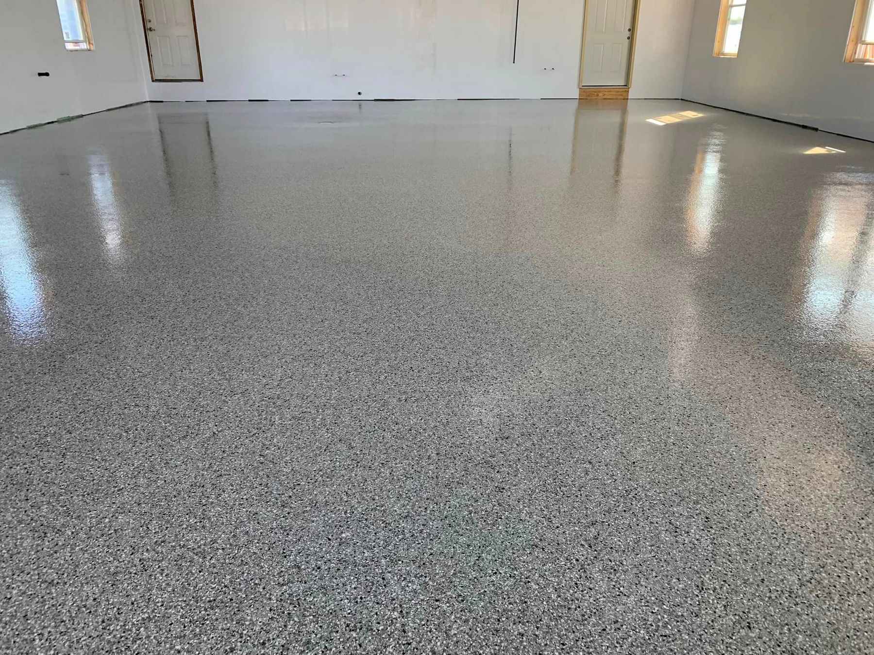 Empty speckled epoxy garage floor with reflections and closed white doors.