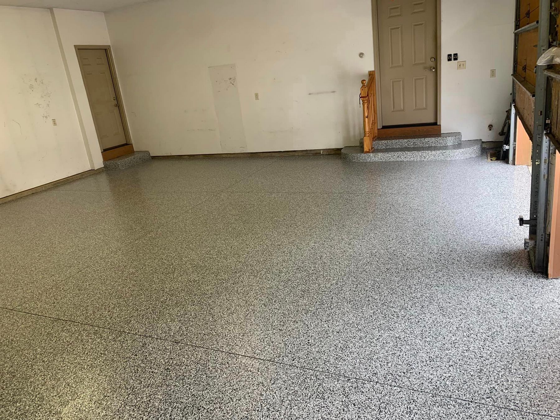 Empty garage with speckled epoxy floor, white walls, and a closed door at the back.