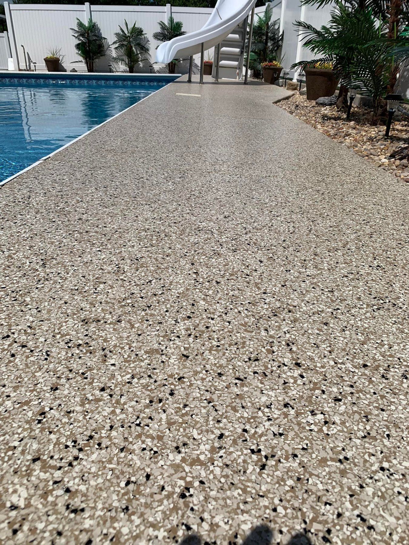 Poolside textured concrete walkway beside blue swimming pool and waterslide
