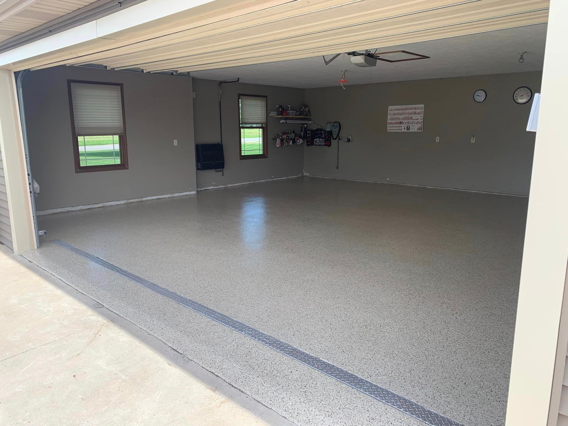 Empty garage with gray walls, speckled epoxy floor, and a partially open door letting in light.
